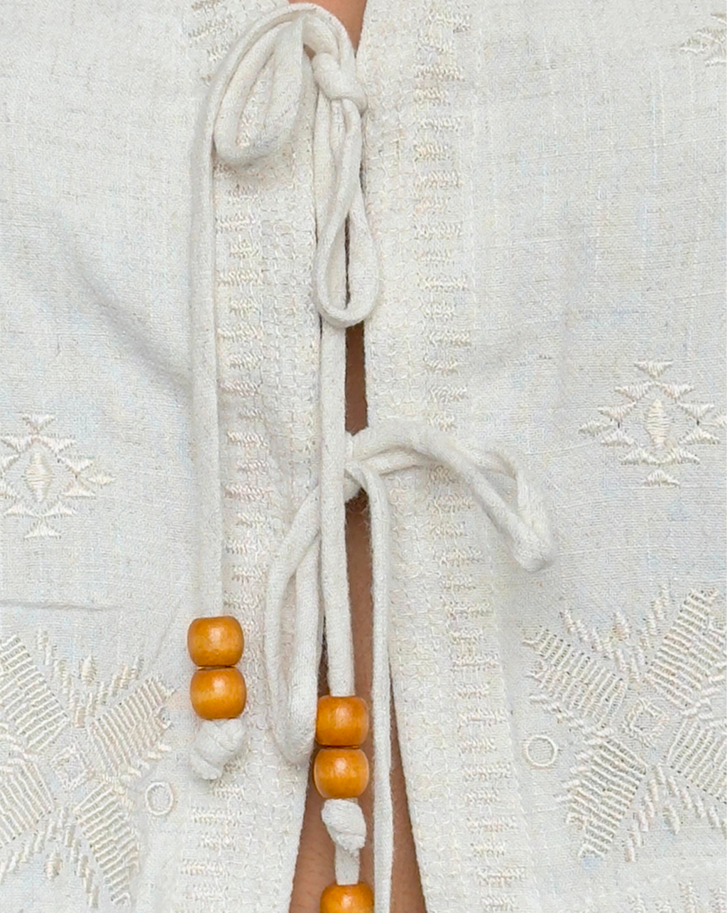 Detalle de blusa color beige en lino, diseño abierto al frente con tiras de tela y cuencas